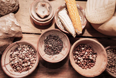 An array of colorful, organic grains, spices, and handmade pottery displayed on a wooden table.
