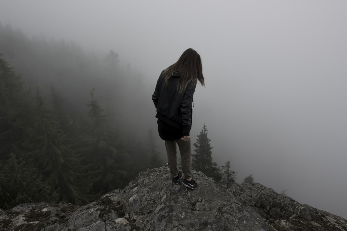 A hiker standing on a dramatic mountain ridge gazing out over a vast moody landscape