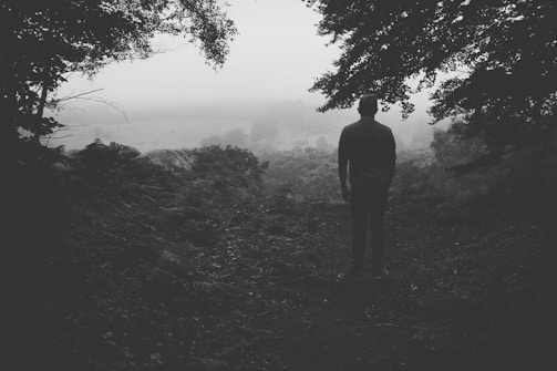 A moody black-and-white portrait of the photographer standing in a misty forest at dawn.
