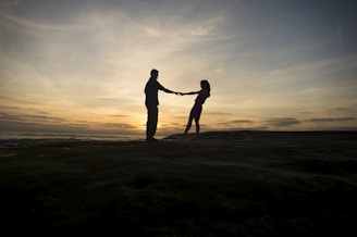 A romantic couple silhouetted against a breathtaking golden sunset, holding hands tenderly.