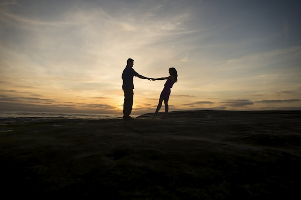 A couple holding hands, silhouetted against a sunset as soft music plays in the background.