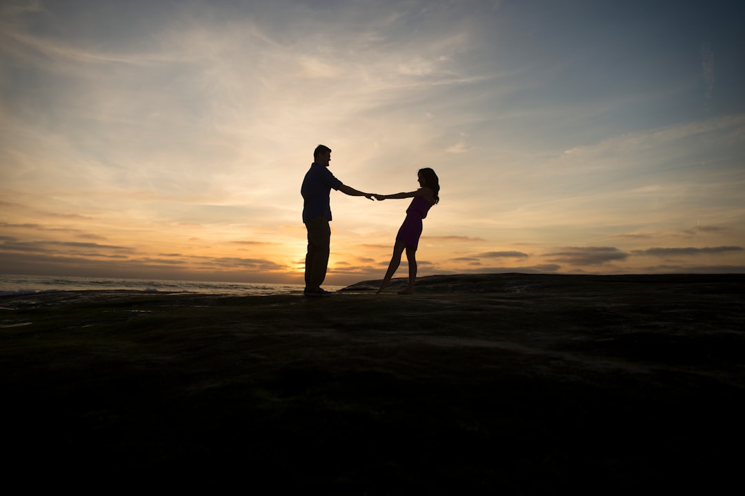 Couple spins round holding hands, silhouetted against setting the sun