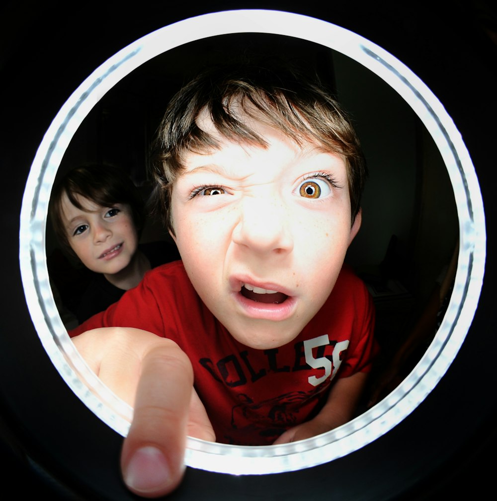 A little boy making a funny face while sticking his finger through a peephole.