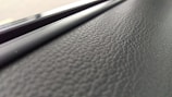 A close-up view of a textured black surface, possibly leather or a similar material, with a glossy, smooth strip running parallel to it.