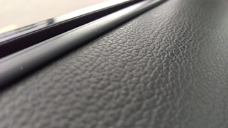 A close-up view of a textured black surface, possibly leather or a similar material, with a glossy, smooth strip running parallel to it.