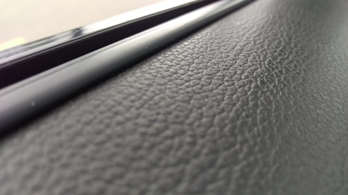 A close-up view of a textured black surface, possibly leather or a similar material, with a glossy, smooth strip running parallel to it.