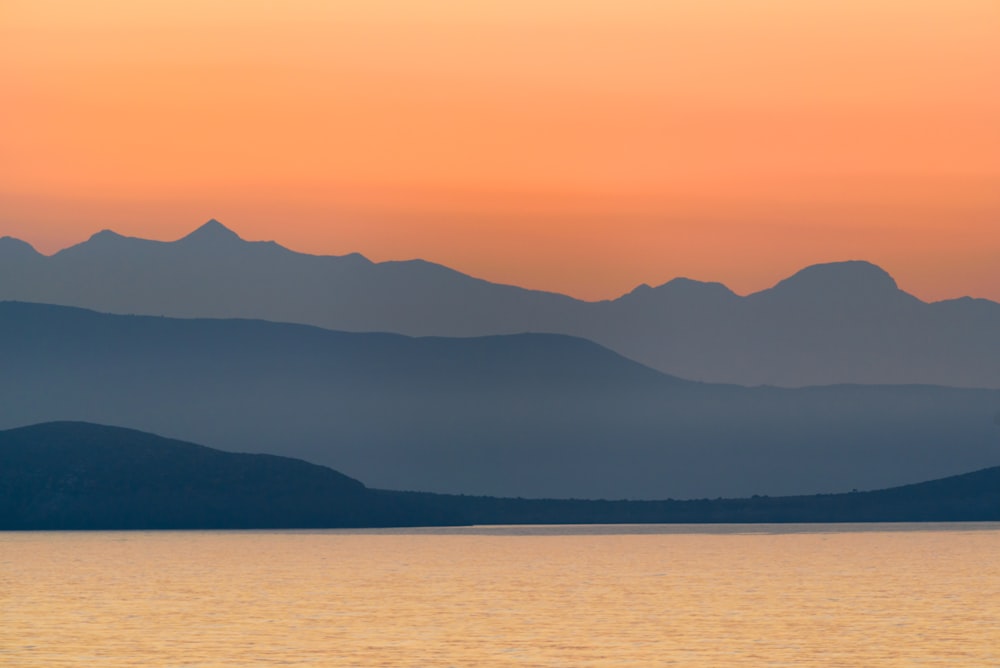 silhouette of mountains near body of water during golden hour