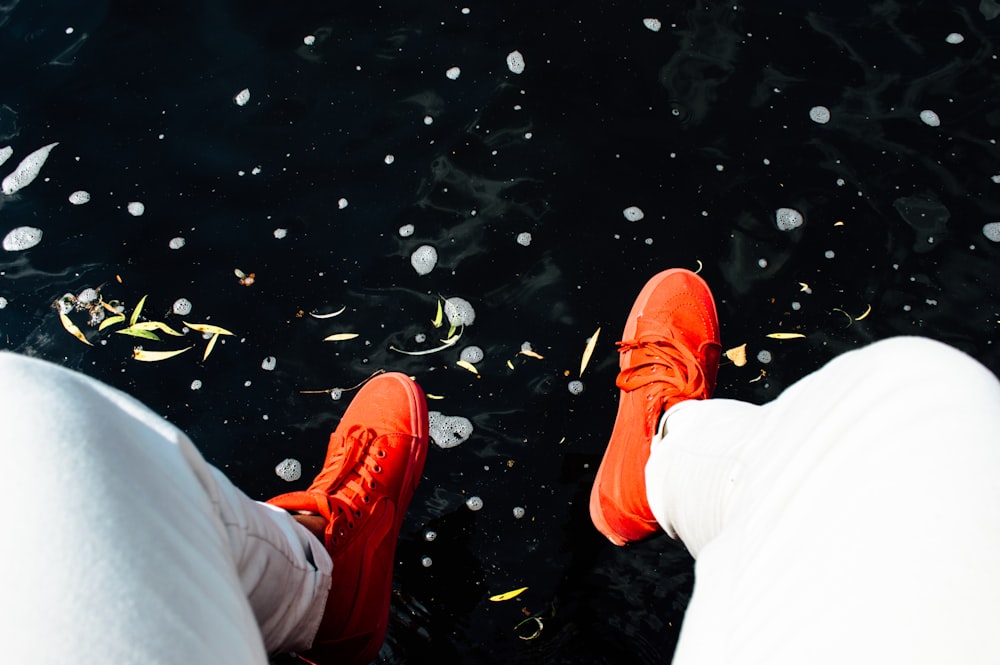 person wearing orange sneakers sitting near water