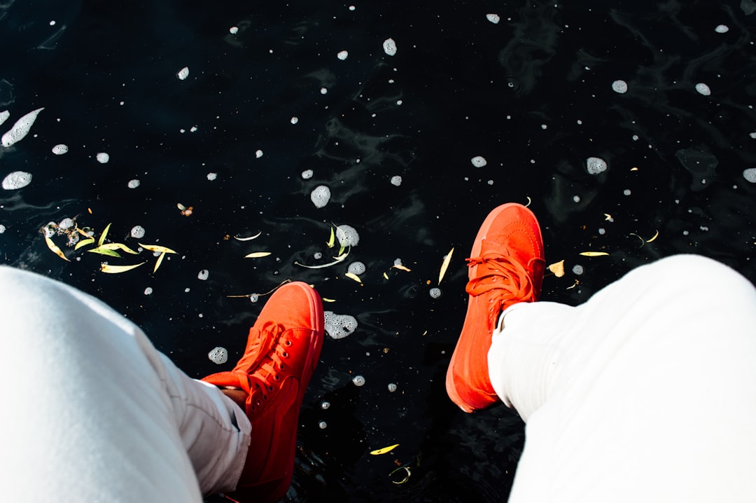 person wearing orange sneakers sitting near water,