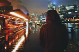 Evening city lights reflecting off a rain-soaked street as a model in a hooded jacket strides confidently.