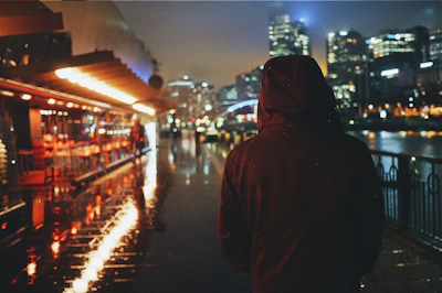 Evening city lights reflecting off a rain-soaked street as a model in a hooded jacket strides confidently.