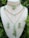 A set of intricately designed jewelry featuring green beads and gold chains is displayed on a mannequin. The set includes two necklaces and a pair of earrings. The necklaces are adorned with green beads, gold chain links, and pendants shaped like hearts and feathers. The earrings have similar green bead and gold accents.