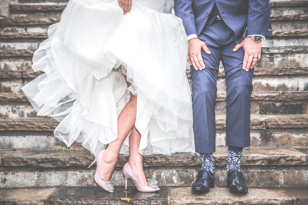 A married couple shows off their wedding dress and suit on steps.