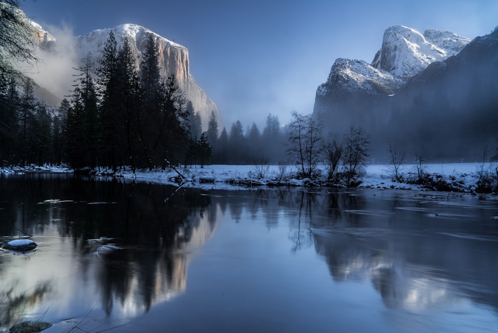 reflection of mountains and trees on body of during snow