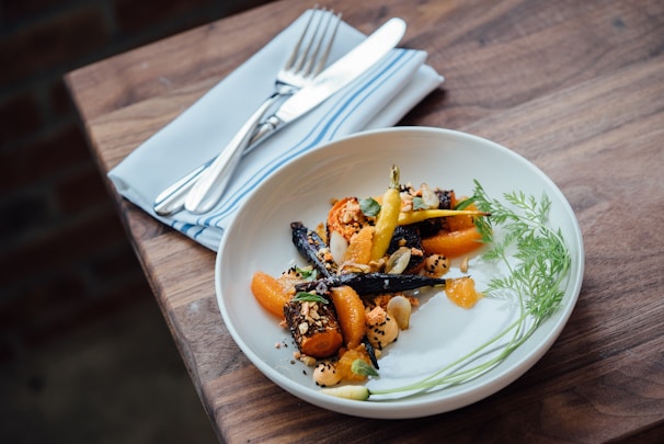 A vibrant vegan plate featuring roasted seasonal vegetables and a drizzle of herb sauce, served on a modern ceramic dish.