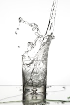 Refreshing splash of water pouring into a glass with Noval Beverages bottle nearby.