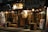 A Japanese restaurant with traditional wooden signage and hanging lanterns, illuminated warmly at night. The exterior includes wooden benches and barrels, with a chalkboard menu at the entrance. Decorative lights are strung along the storefront, adding to the inviting ambiance.