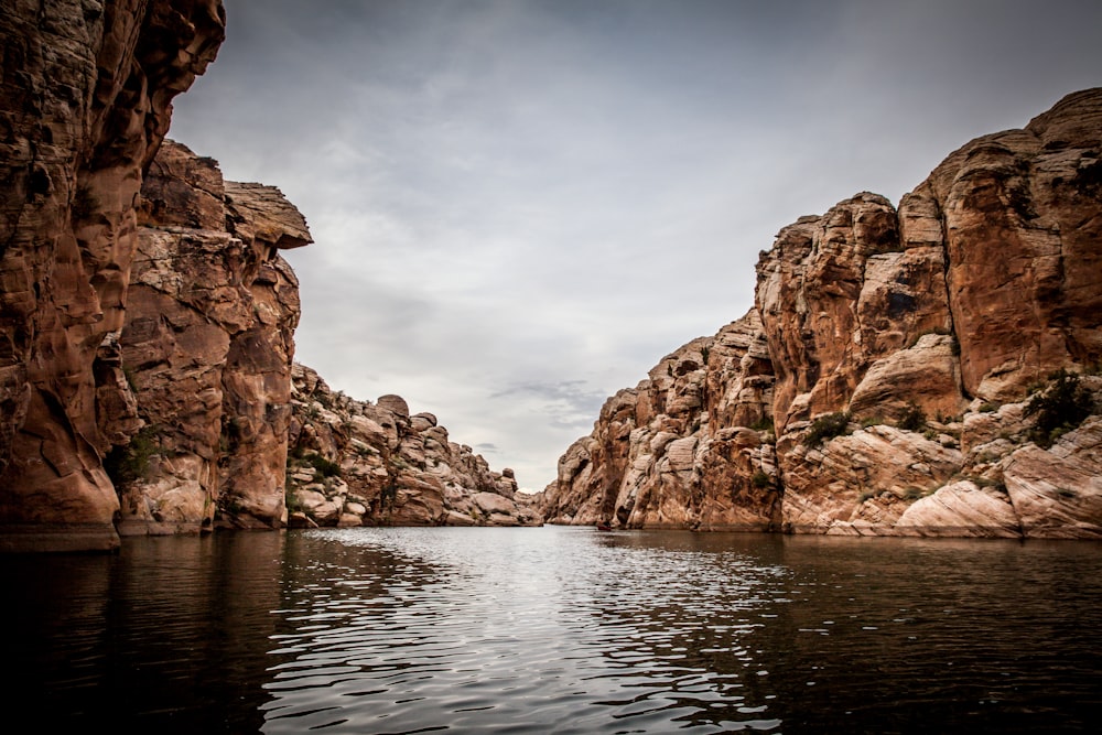 brown cliffs in front of body of water during cloudy sky