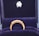A gold ring with a row of small, sparkling diamonds is prominently displayed against a plush, dark blue velvet background. The ring appears elegant and is encased in a box lined with the same blue velvet, suggesting it is a piece of fine jewelry.