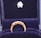 A gold ring with a row of small, sparkling diamonds is prominently displayed against a plush, dark blue velvet background. The ring appears elegant and is encased in a box lined with the same blue velvet, suggesting it is a piece of fine jewelry.