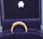 A gold ring with a row of small, sparkling diamonds is prominently displayed against a plush, dark blue velvet background. The ring appears elegant and is encased in a box lined with the same blue velvet, suggesting it is a piece of fine jewelry.
