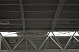 A metal roof structure with exposed beams and crossbars, featuring visible light fixtures attached to the ceiling. The structure has a utilitarian and industrial aesthetic.