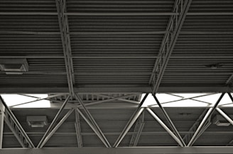 A metal roof structure with exposed beams and crossbars, featuring visible light fixtures attached to the ceiling. The structure has a utilitarian and industrial aesthetic.
