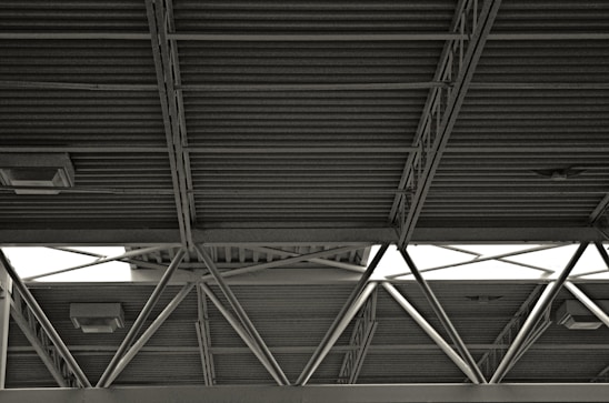 A metal roof structure with exposed beams and crossbars, featuring visible light fixtures attached to the ceiling. The structure has a utilitarian and industrial aesthetic.
