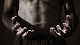 Close-up of a male athlete's sculpted arm under dramatic chiaroscuro lighting.