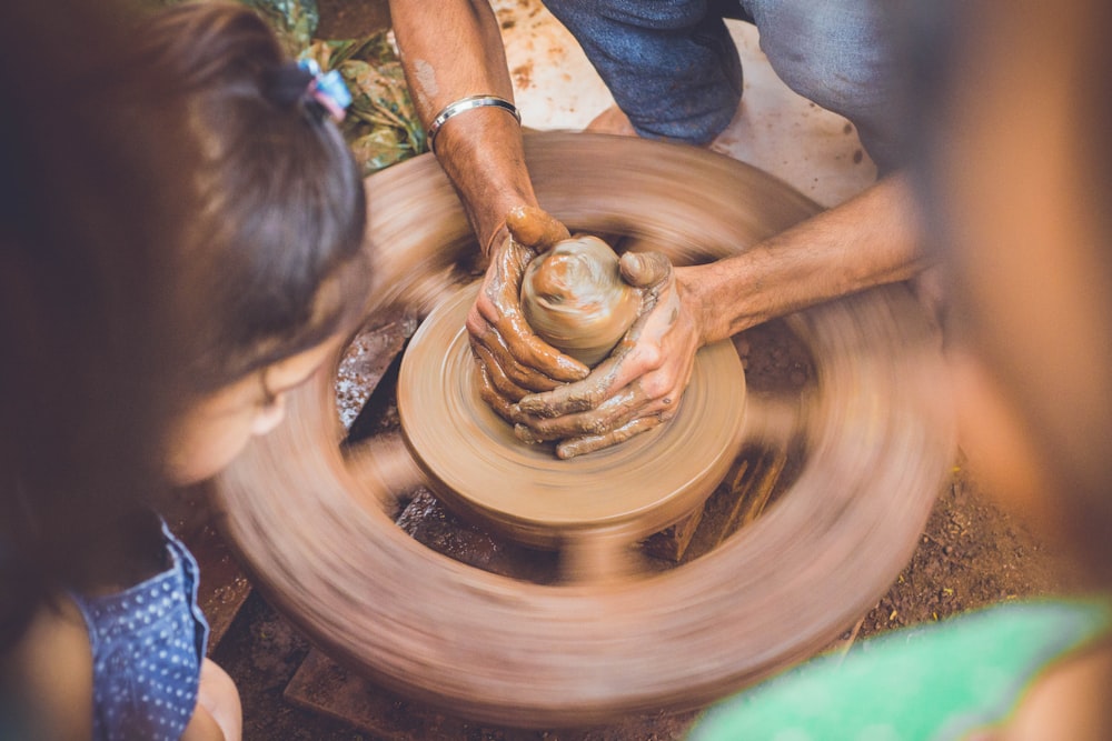 person molding clay while children are watching at daytime