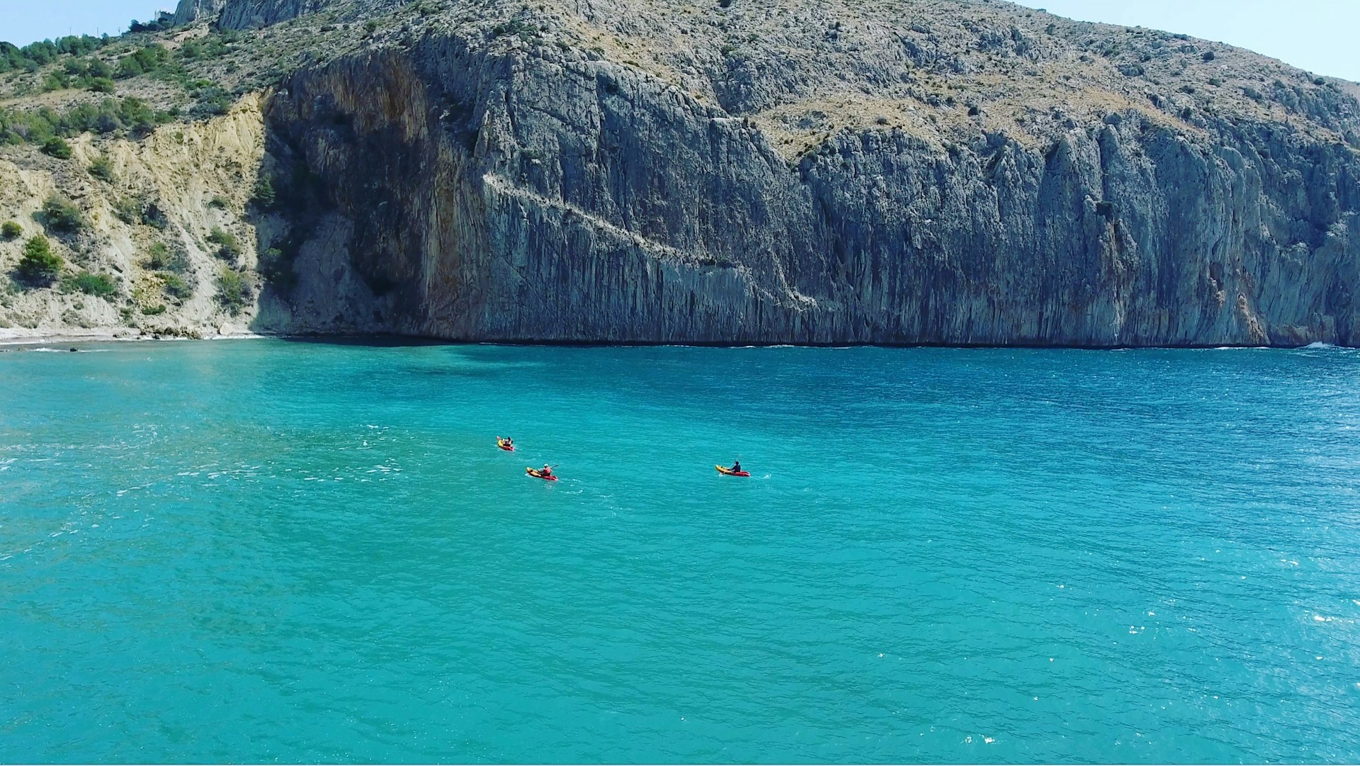 An adventurous scene of a group kayaking through sparkling turquoise ocean waters, framed by dramatic coastal cliffs under radiant sunlight.