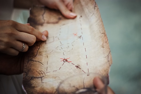 a hand touching a stop on a treasure map with frayed edges