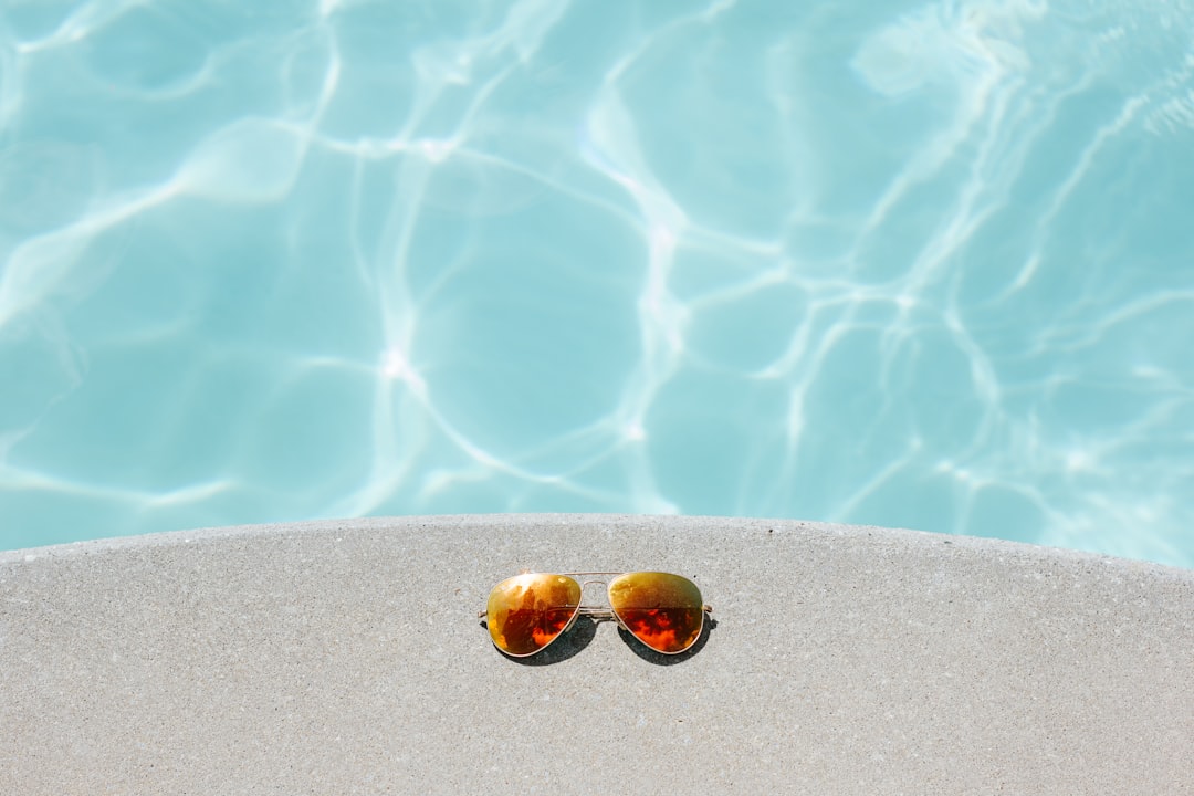 gold framed orange lens Aviator-style sunglasses beside pool, Reflective sunglasses