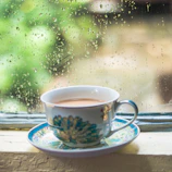 A steaming cup of tea on a wooden table by a window with raindrops outside