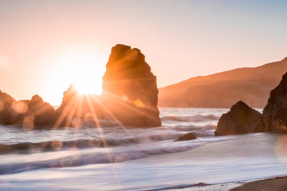 golden hour photography of rock formation on body of water