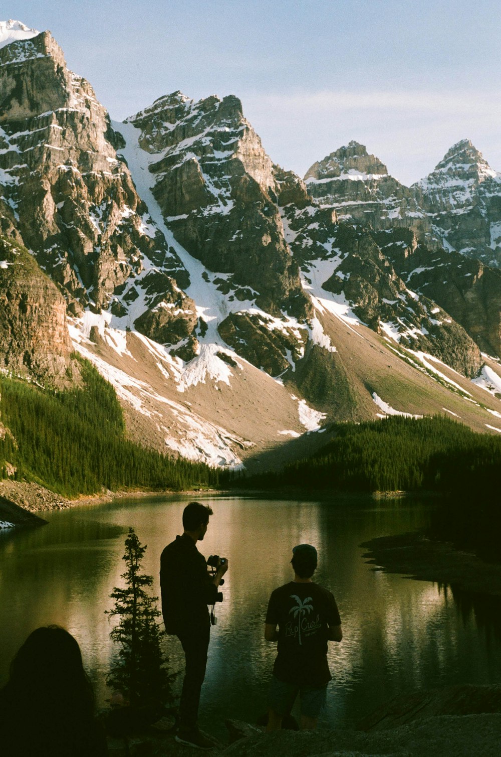 two men standing near body of water and mountain