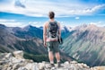 man standing on cliff facing mountain range