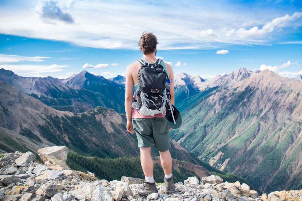 man standing on cliff facing mountain range