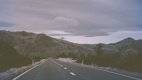 An open road stretching into the horizon, framed by rugged terrain and a moody, overcast sky.