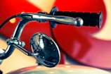 Close-up of biker's hand gripping a skull-emblazoned motorcycle handlebar under red neon light.