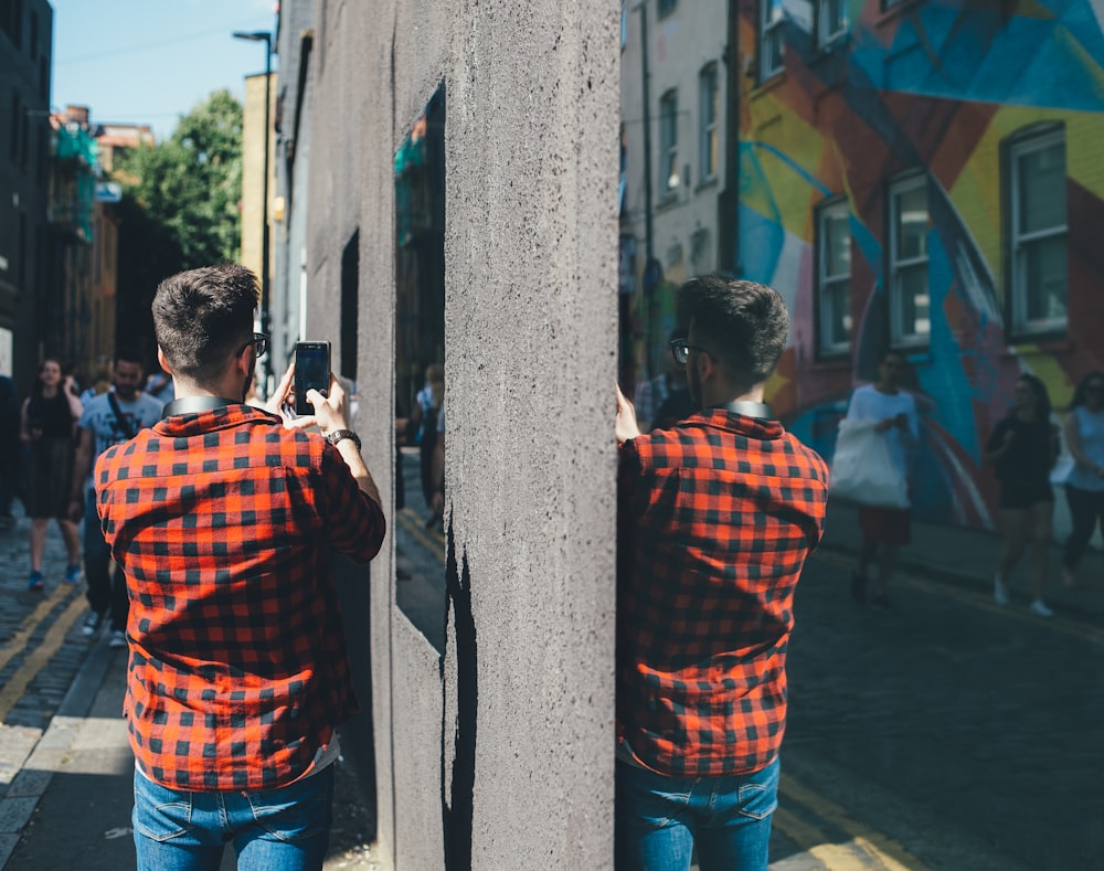 shallow focus photo of person in red and black plaid shirt holding black smartphone