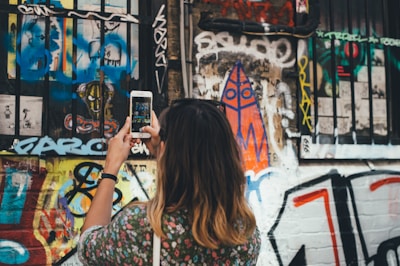 Close-up of a trendy Asian influencer filming a TikTok video with colorful urban graffiti behind.