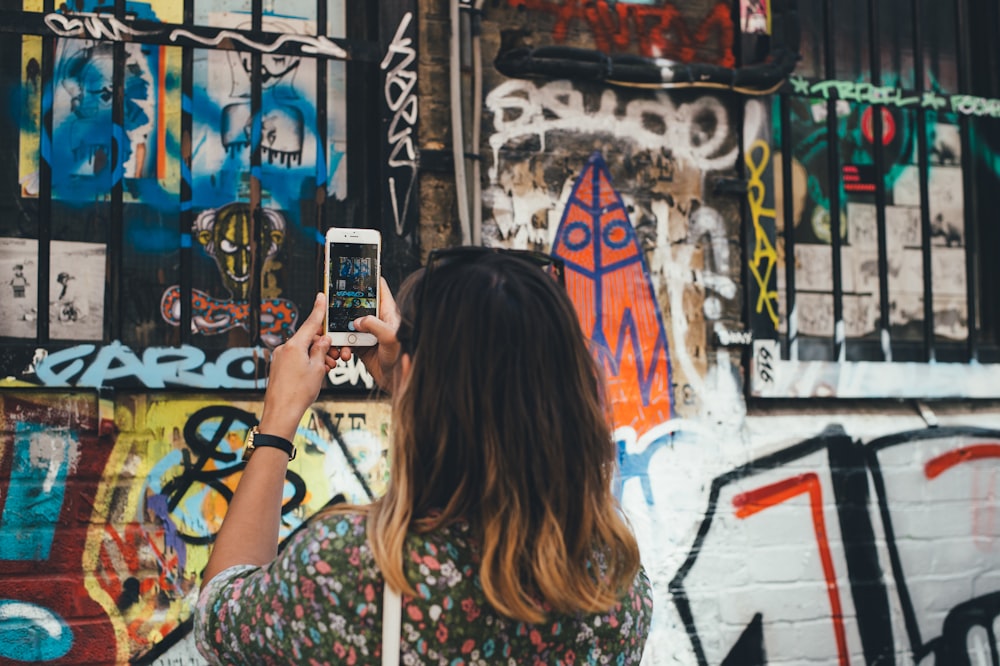 Mujer sosteniendo el teléfono tomando una foto en la pared