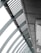 A perspective view of an architectural structure showcasing a series of curved steel beams forming an arc. The beams are complemented by slatted panels and lights attached along the interior. The image features a modern, industrial design with a focus on geometric lines and patterns.
