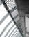 A perspective view of an architectural structure showcasing a series of curved steel beams forming an arc. The beams are complemented by slatted panels and lights attached along the interior. The image features a modern, industrial design with a focus on geometric lines and patterns.