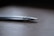 A close-up view of a pair of metallic tweezers with a sleek design lying on a wooden surface. The focus is on the pointed end, showcasing the fine tips and reflective surface.