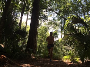 A woman jogging on a forest trail with sunlight filtering through the trees