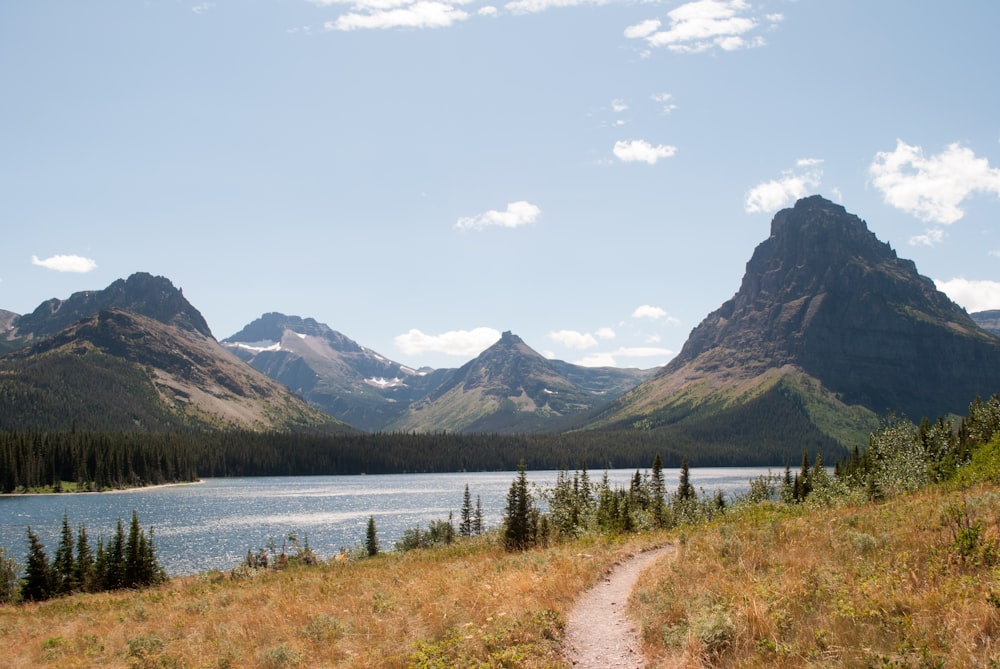 lake near green grass field and mountains under white clouds during daytime