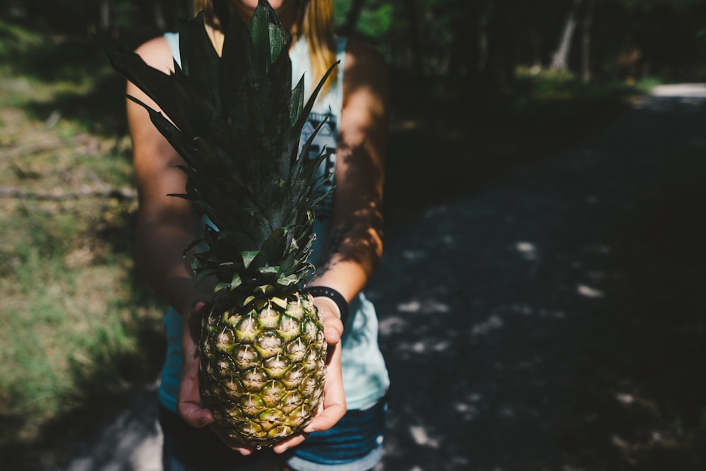 person standing on gray pavement carrying pineapple fruit