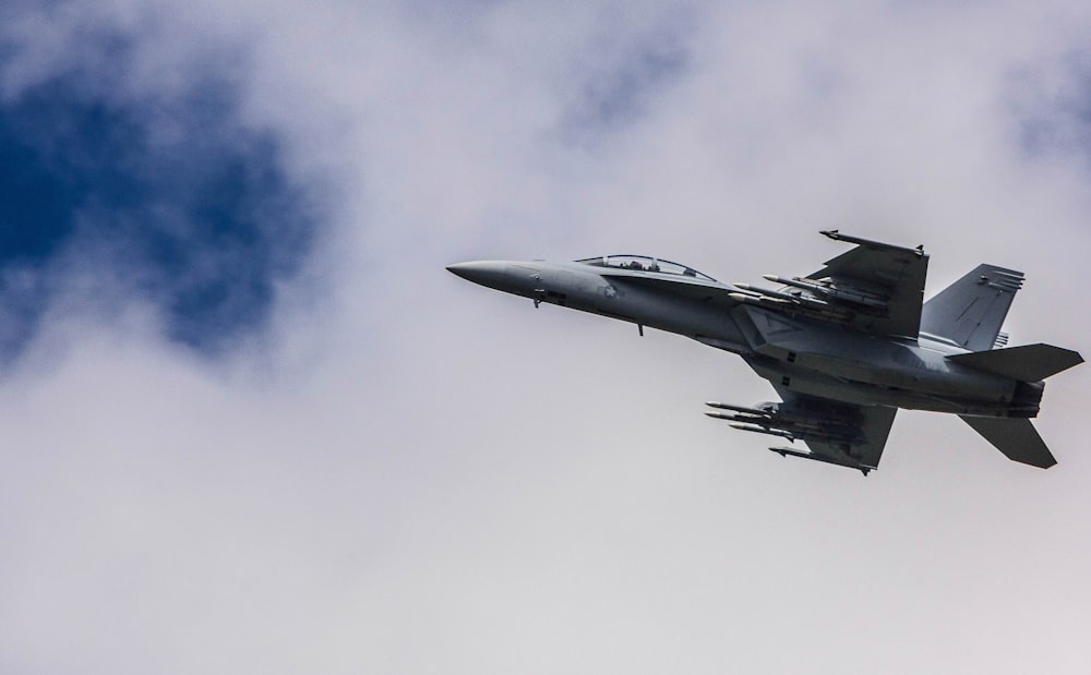 Kampfjet fliegt unter weißen Wolken